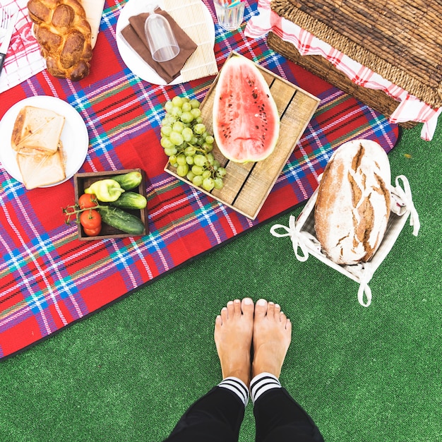 Primer plano de los pies de la mujer cerca de la merienda de picnic en una manta