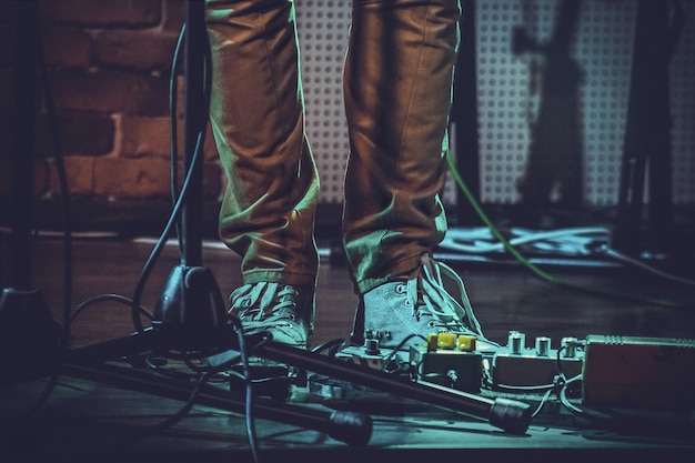 Primer plano de los pies de una persona cerca de los pedales de guitarra y un soporte de micrófono bajo las luces
