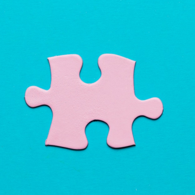Primer plano de pieza de rompecabezas de color rosa sobre fondo azul
