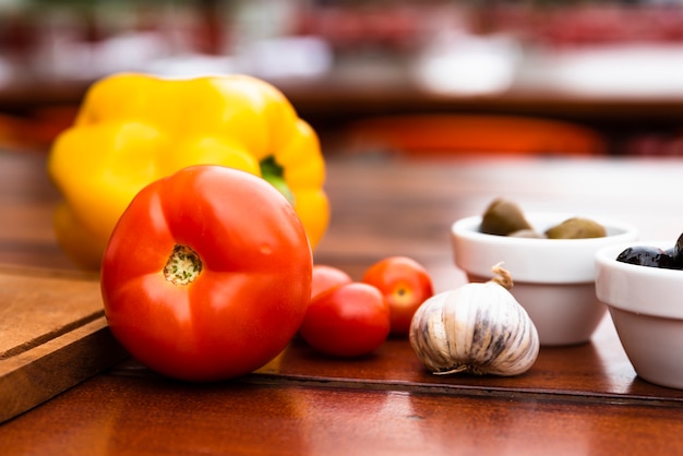 Primer plano de pimiento amarillo; tomates Bulbo de ajo y tazón de aceitunas en mesa de madera