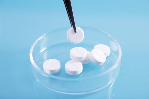 Primer plano de pinzas recogiendo una pastilla blanca de un montón en un plato de vidrio en un laboratorio