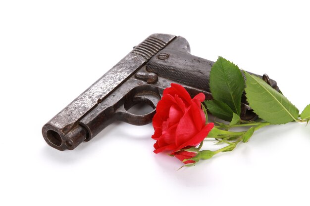 Primer plano de una pistola y una rosa roja aislado sobre un fondo blanco.
