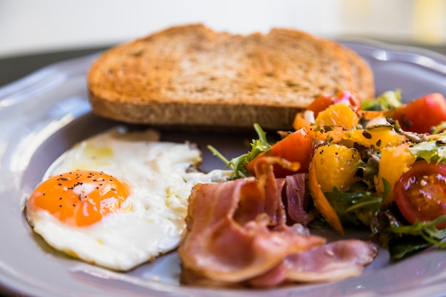 Foto gratuita primer plano de la placa gris con pan tostado; huevos fritos; tocino y ensalada