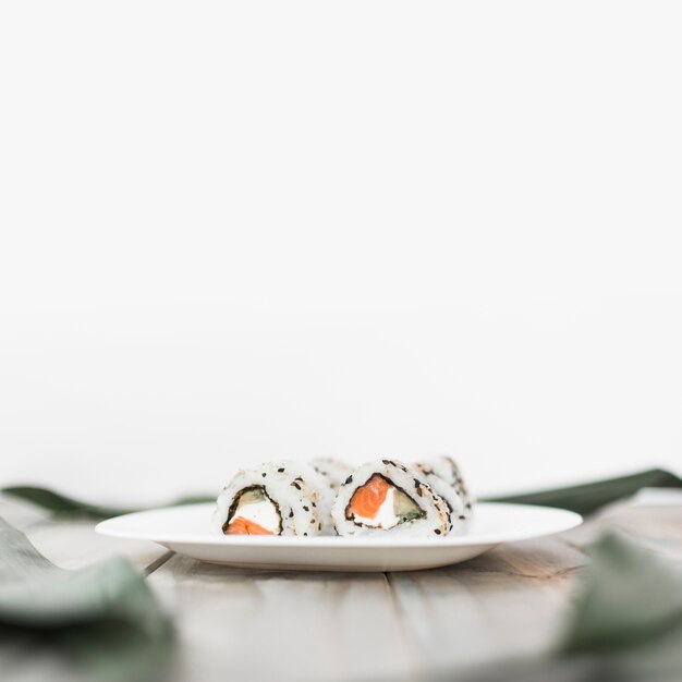 Primer plano de un plato blanco con sushi en una mesa de madera con fondo blanco
