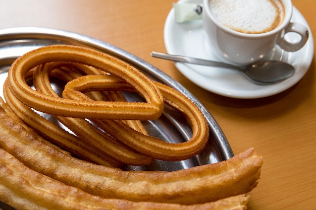 Primer plano de un plato con churros y una taza de café