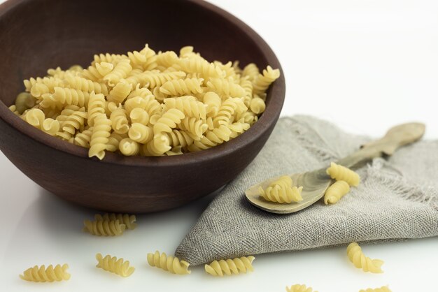 Primer plano de un plato de pasta fusilli con una cuchara de madera sobre una tela gris