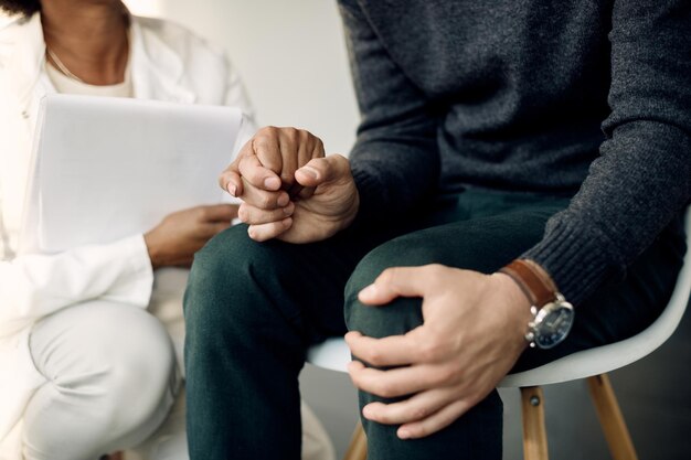 Primer plano de un psicoterapeuta de apoyo sosteniendo la mano de un paciente ansioso