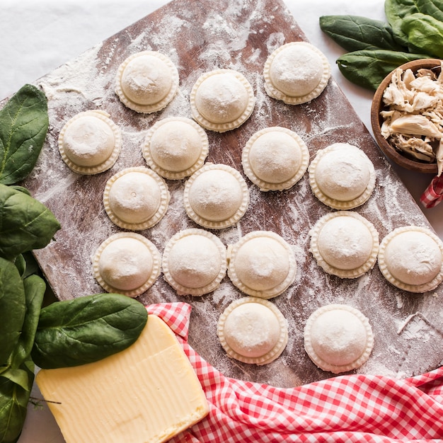 Foto gratuita primer plano de raviolis crudos espolvoreados con harina en tablero de madera con ingredientes