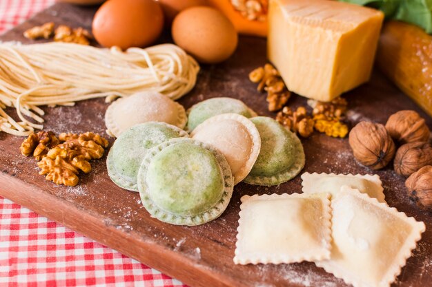 Primer plano de raviolis crudos con ingredientes en tabla de cortar de madera