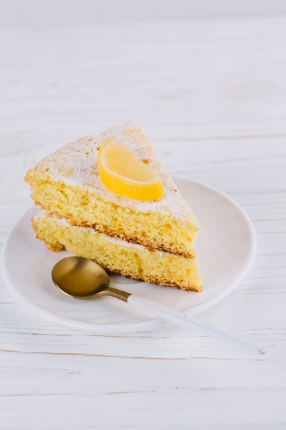 Primer plano de una rebanada decorada de la torta del limón en la placa blanca con la cuchara