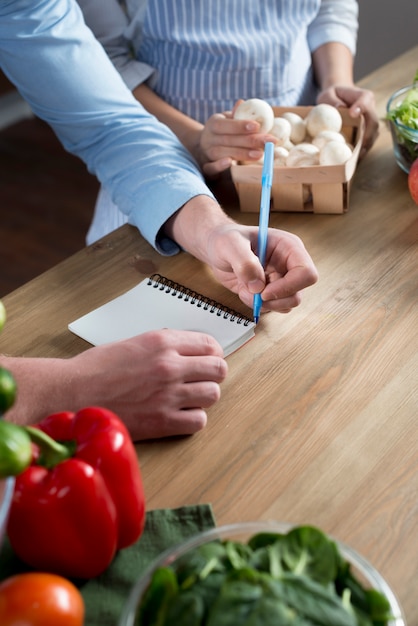 Primer plano de la receta de escritura de mano del hombre en el diario en el mostrador de la cocina de madera