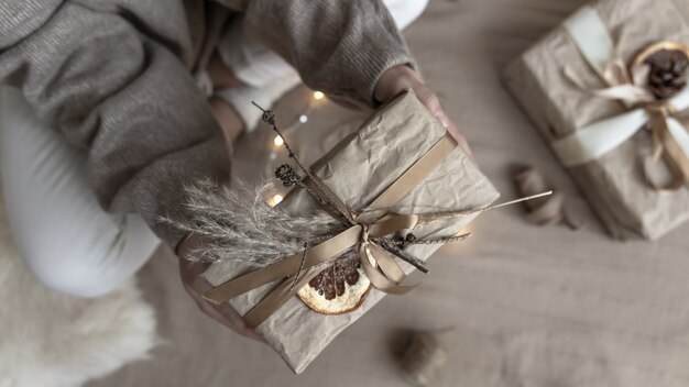 Primer plano de un regalo de Navidad, decorado con flores secas y una naranja seca, envuelto en papel artesanal.