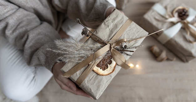 Primer plano de un regalo de Navidad, decorado con flores secas y una naranja seca, envuelto en papel artesanal.