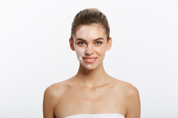 Primer plano retrato de belleza de hermosa mujer semidesnuda aplicando crema facial aislada sobre respaldo blanco