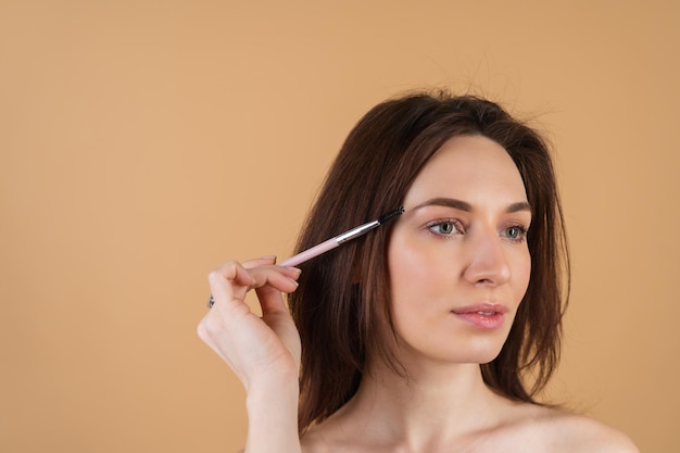 Primer plano retrato de belleza de una mujer con piel perfecta y maquillaje natural, labios brillantes, sosteniendo un cepillo de cejas