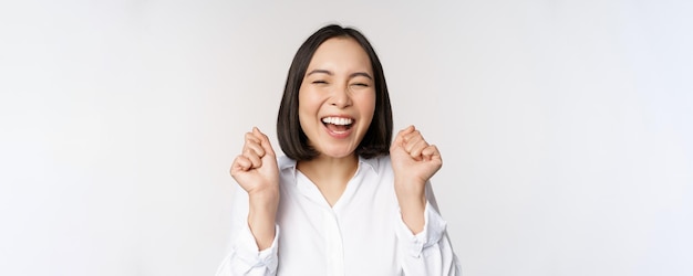 Primer plano retrato de cara de mujer asiática bailando sonriendo triunfando y celebrando con emoción feliz de pie sobre fondo blanco Copiar espacio