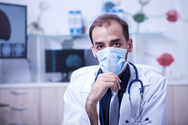 Primer plano retrato de cirujano médico hombre usar máscara quirúrgica. Médico joven serio en su gabinete en la clínica.