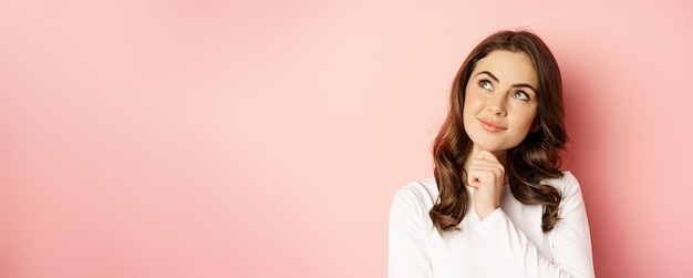 Foto gratuita primer plano retrato de coqueta mujer sonriente glamour chica pensando mirando pensativo de pie sobre fondo rosa