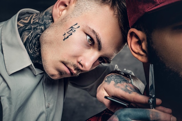 Primer plano retrato de cortes de peluquero masculino tatuado, barba a un hombre negro.