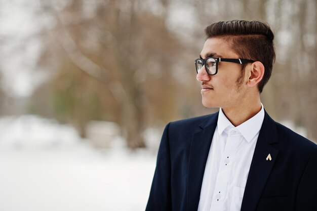 Primer plano retrato de un elegante estudiante indio con traje y gafas posado en el día de invierno al aire libre