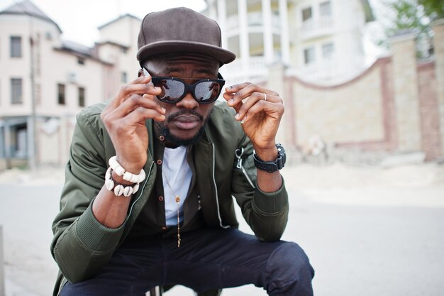 Primer plano retrato de elegante hombre afroamericano usar gafas de sol y gorra al aire libre Street fashion black man