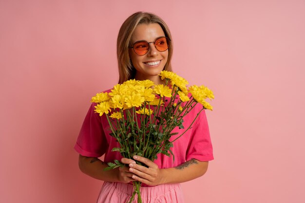 Primer plano retrato de estudio og Alegre linda mujer rubia sosteniendo flores de primavera sobre fondo rosa