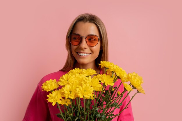 Primer plano retrato de estudio og Alegre linda mujer rubia sosteniendo flores de primavera sobre fondo rosa