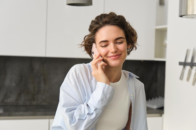 Primer plano retrato de hermosa chica europea con teléfono inteligente sentado en casa y hablando por móvil p