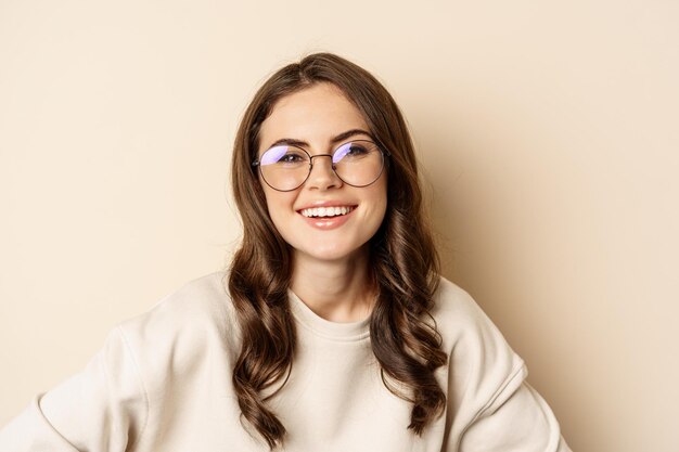 Primer plano retrato de hermosa mujer moderna con gafas sonriendo y luciendo feliz posando en anteojos y...