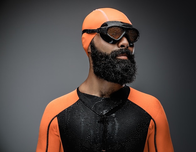 Primer plano retrato de hombre barbudo en máscara de buceo y traje de buceo de neopreno naranja aislado sobre fondo gris.