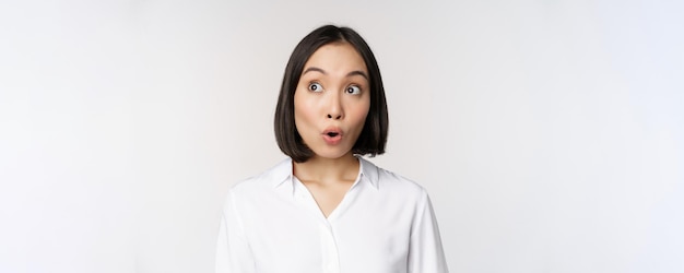 Primer plano retrato de una joven asiática haciendo una cara sorprendida mirando la esquina superior izquierda impresionada emoción wow de pie sobre fondo blanco