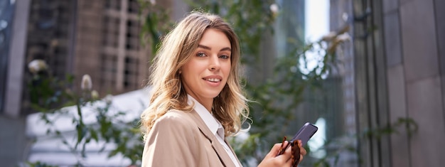 Foto gratuita primer plano retrato de una joven empresaria sonriente en traje sosteniendo un teléfono inteligente y