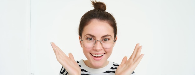 Foto gratuita primer plano retrato de una joven feliz y asombrada con gafas apretando las manos aplaudiendo y sonriendo