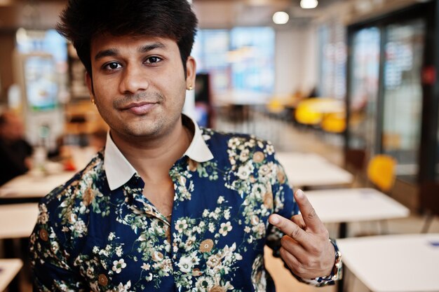 Primer plano retrato de un joven independiente indio masculino en un café de comida rápida guapo cabeza de hombre asiático vestido con camisa en una cómoda cafetería muestra el signo de dos dedos