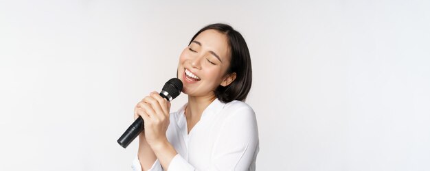 Primer plano retrato de mujer asiática cantando en el micrófono en el karaoke de pie sobre fondo blanco.