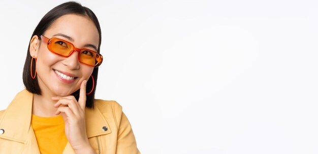 Primer plano retrato de mujer asiática pensando con gafas de sol y sonriendo mirando hacia arriba pensativo stand