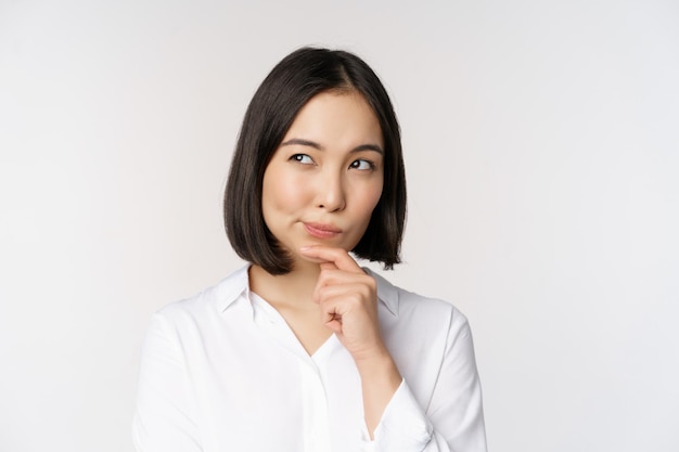 Primer plano retrato de mujer asiática pensando mirando a un lado y reflexionando sobre la toma de decisiones de pie sobre fondo blanco