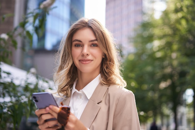 Foto gratuita primer plano retrato de mujer corporativa joven pasante camina en la calle a la oficina tiene mensajes de texto de teléfono móvil