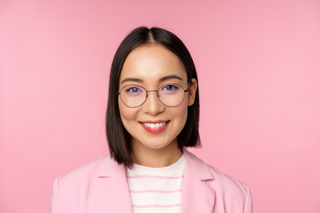 Primer plano retrato de mujer empresaria profesional asiática empresaria en gafas sonriendo y mirando con confianza a la cámara fondo rosa