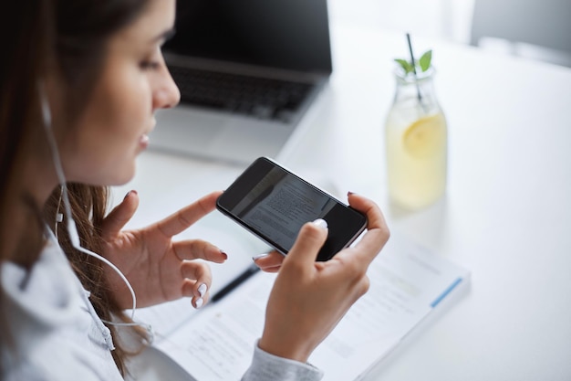 Primer plano retrato de una mujer joven perfecta que usa un teléfono inteligente para hacer hojas de trucos para su futuro examen bebiendo limonada de limones que le dio la vida