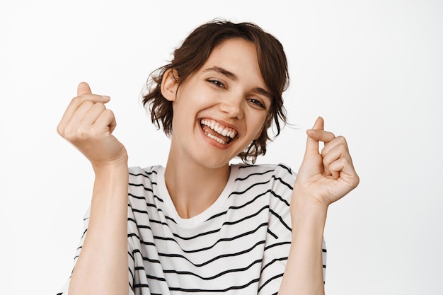 Primer plano retrato de mujer morena feliz, bailando y riendo, sonriendo dientes blancos, de pie en camiseta contra fondo blanco.