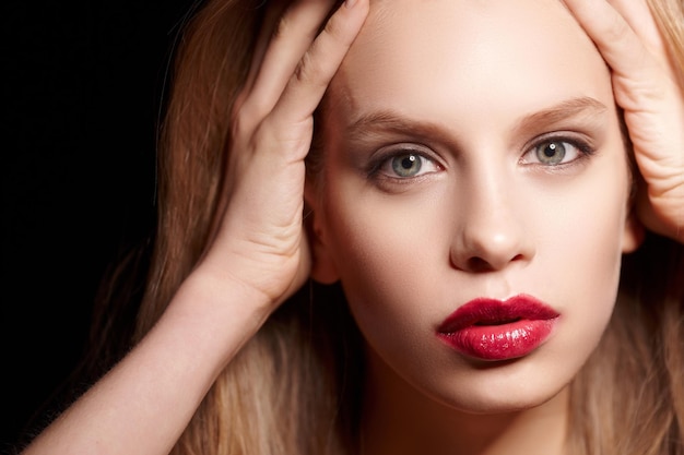 Primer plano retrato de mujer rubia con labios rojos aislado sobre fondo negro.