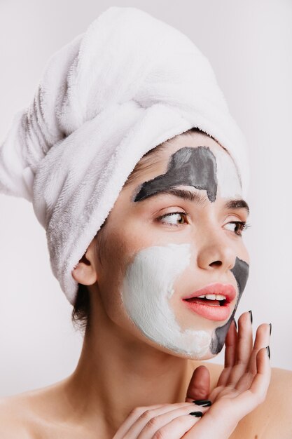 Primer plano de retrato de niña bonita con toalla sobre el cabello mojado. Mujer con mascarilla posando en pared aislada.