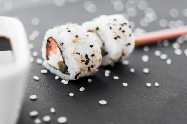 Primer plano de rollo de sushi con semillas de sésamo y arroz crudo sobre fondo negro con textura