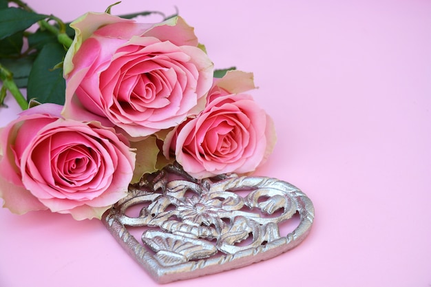 Primer plano de rosas rosadas con forma de corazón metálico sobre una superficie rosa
