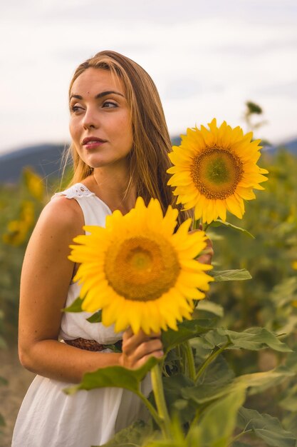 Primer plano de una rubia con un vestido blanco posando en un campo de girasoles