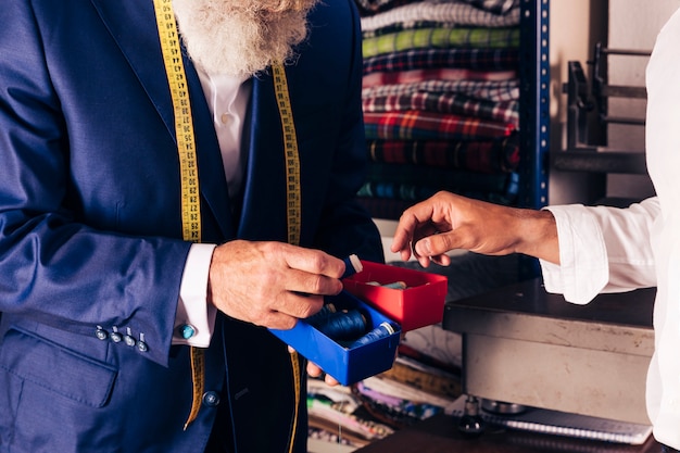 Primer plano de un sastre masculino que muestra un carrete de hilo a su cliente