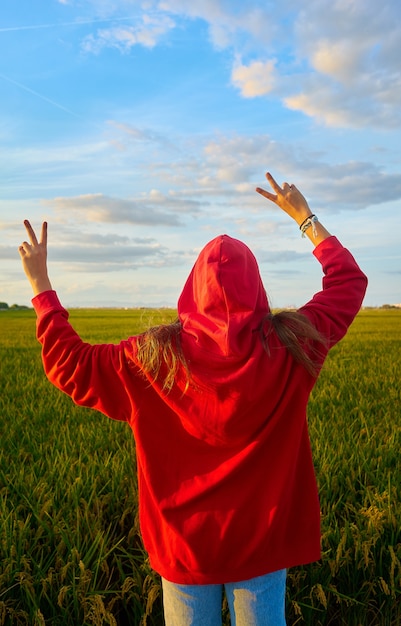 Primer plano de una señorita en rojo alegremente de pie en un campo verde en un día soleado