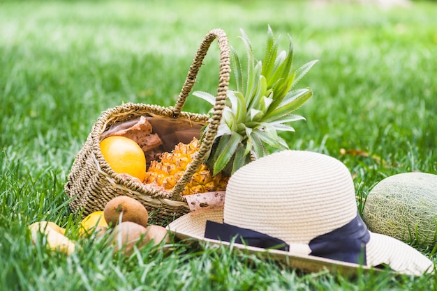 Primer plano de sombrero y frutas en cesta de mimbre sobre hierba