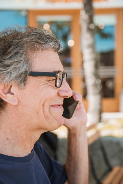 Foto gratuita primer plano de sonrientes lentes de hombre senior vistiendo hablando por teléfono celular